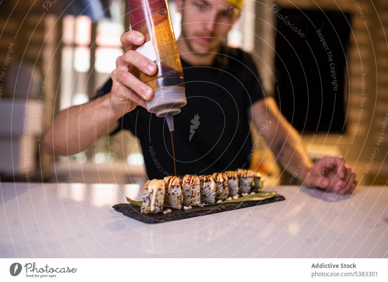 Serious young man adding sauce on gunkan maki cook concentrate delicious garnish tasty counter sushi prepare kitchen japanese male chef asian food restaurant