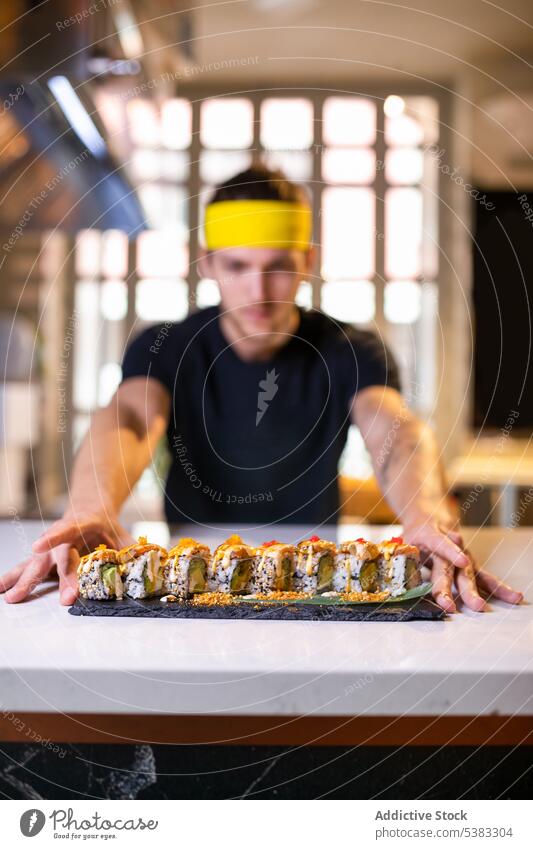 Young man presenting tray with uramaki sushi rolls on table avocado rice serve delicious food kitchen young male asian food japanese tasty cuisine meal fresh