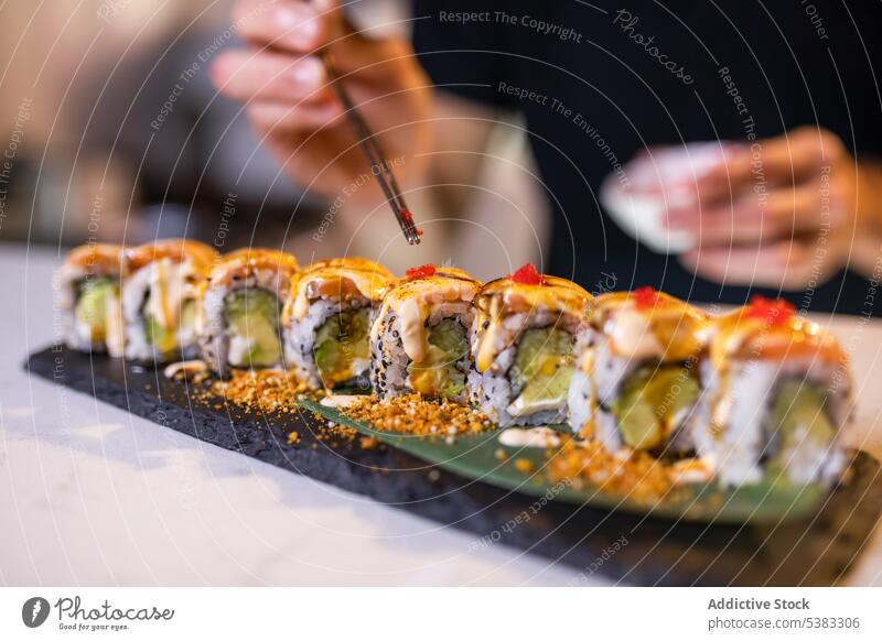 Unrecognizable person serving tobiko on uramaki sushi rolls with chopsticks anonymous rice serve seafood tray delicious avocado asian food meal tasty cuisine