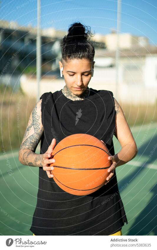 Cool serious woman holding basketball ball on playground sportswoman player streetball tattoo training masculine brutal androgynous game sportswear female court