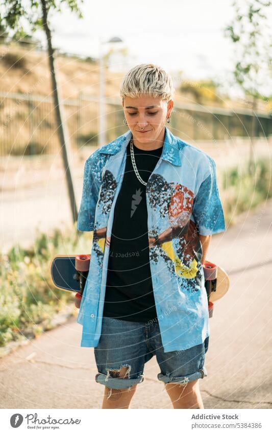 Smiling shy tomboy with skateboard in park woman street androgynous positive smile skater casual trendy young female happy pride cool carefree modern charming
