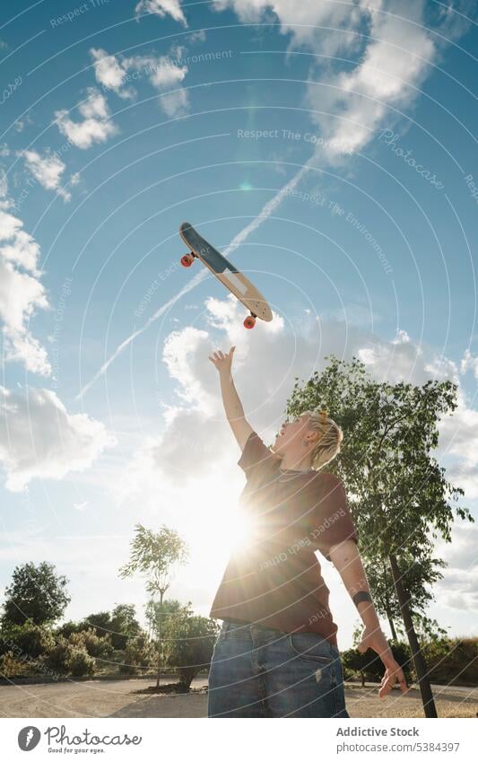 Excited tomboy throwing skateboard in sky woman excited toss androgynous arm raised achieve fun joy cloudy blue sky countryside activity young pride casual
