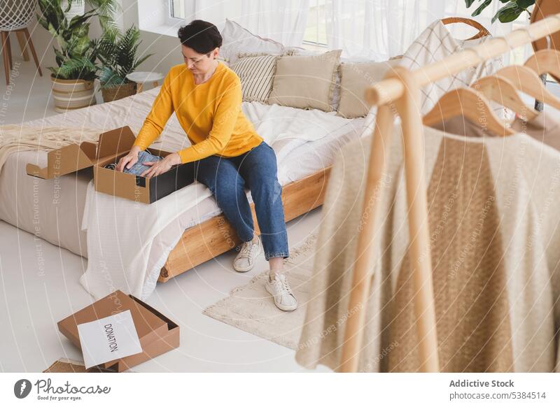 Focused woman packing clothes for donation focus concentrate donate charity package box at home calm bedroom pensive apartment relocate sit casual prepare