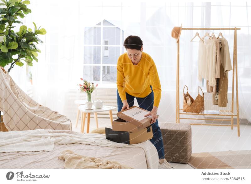 Woman packing boxes in light bedroom woman concentrate focus donation donate charity at home cloth hanger apartment female mature casual prepare sweater jeans