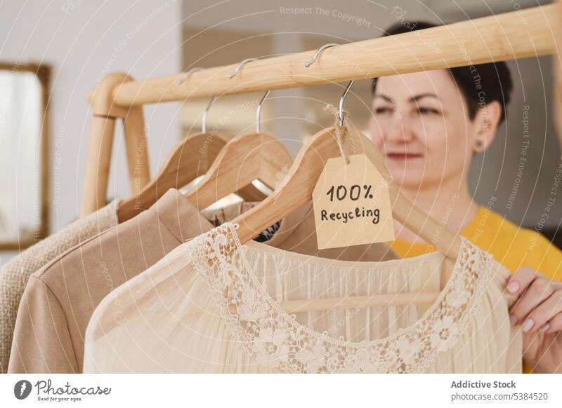 Blurred female near clothes hanging on wooden hangers rack inscription recycle garment tag label zero waste apparel minimal design light material inside textile