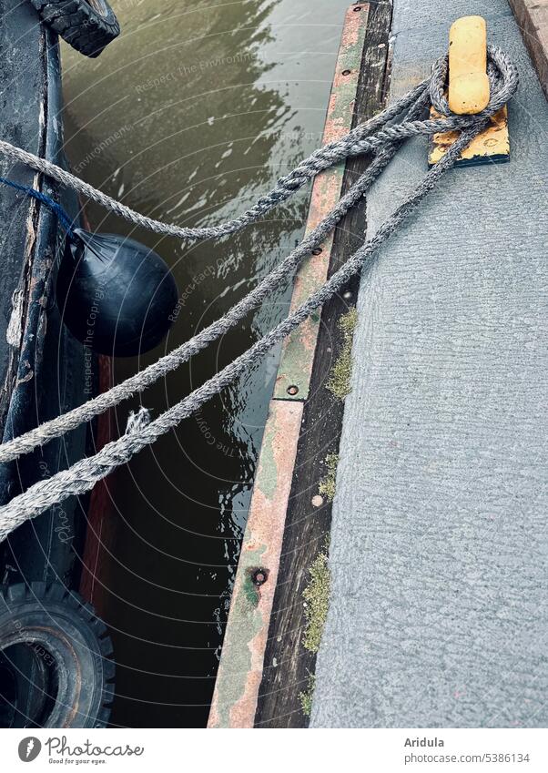 Boat with fender and car tire to starboard moored with lines to yellow bollard boat Cutter Footbridge Harbour Bollard leash Fender Car tire Starbord Water Rope