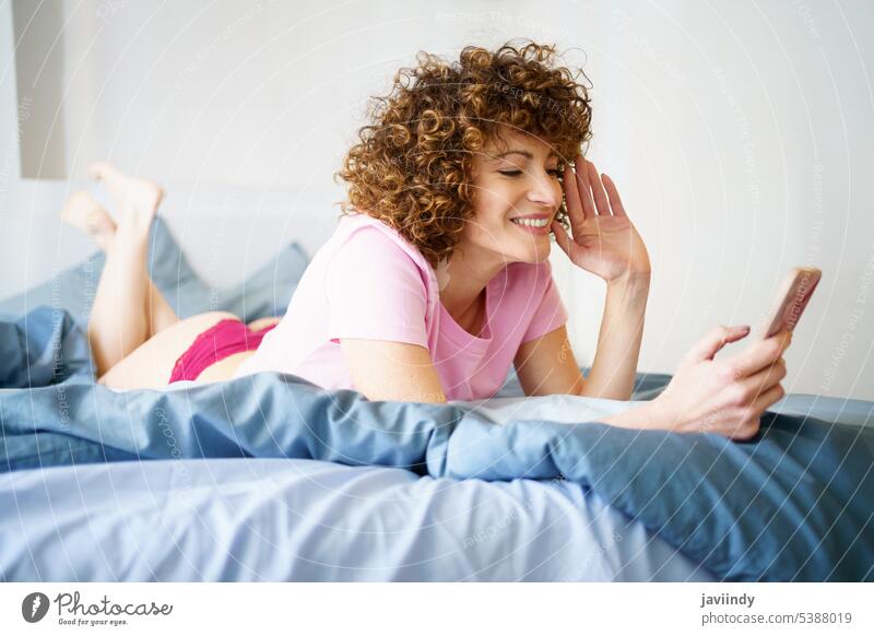 Smiling woman talking on video chat via smartphone in bed wave hand video call using smile greeting connection social media home happy gadget female device