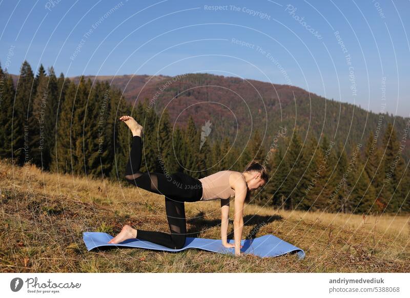Young fit woman doing exercises on yoga mat on background of sunny mountains hills. Outdoor workout, healthy lifestyle. female in sport suit doing asanas in nature against the forest in the morning