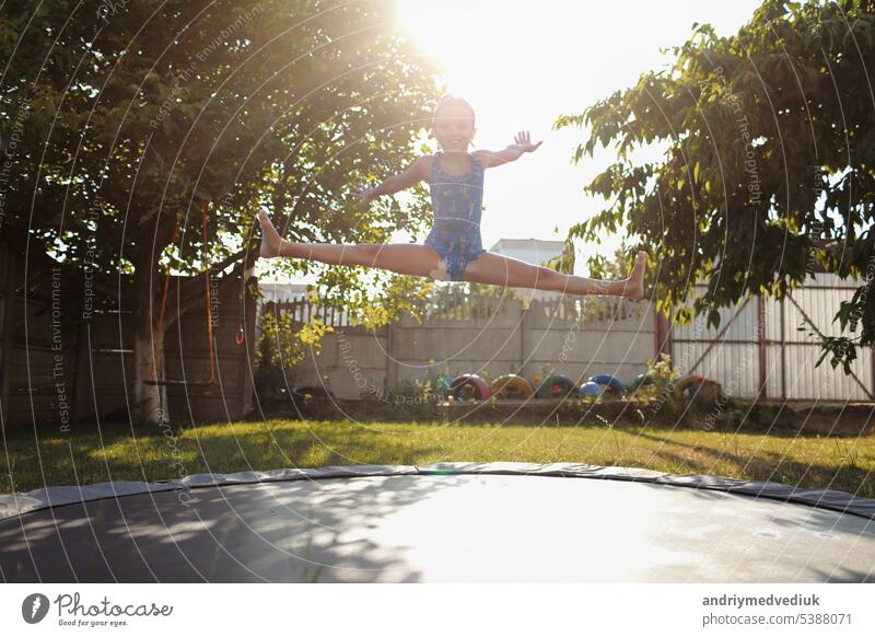 little sports girl jumps on a trampoline. Outdoor shot of girl jumping on trampoline, enjoys jumping in home. happy summer vacation child fitness kid nature sun