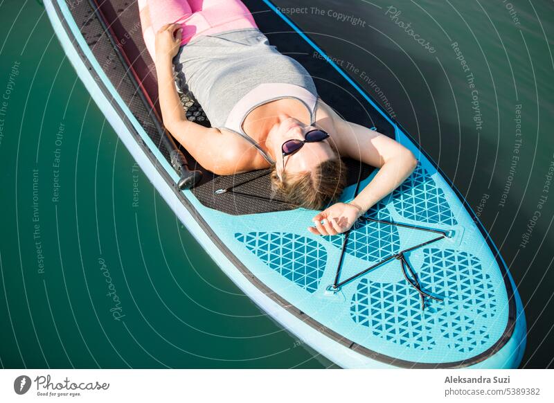 Young athletic woman paddling along the river lying on the sup board, relaxing under summer sun active activity adventure attractive beach beautiful boarding