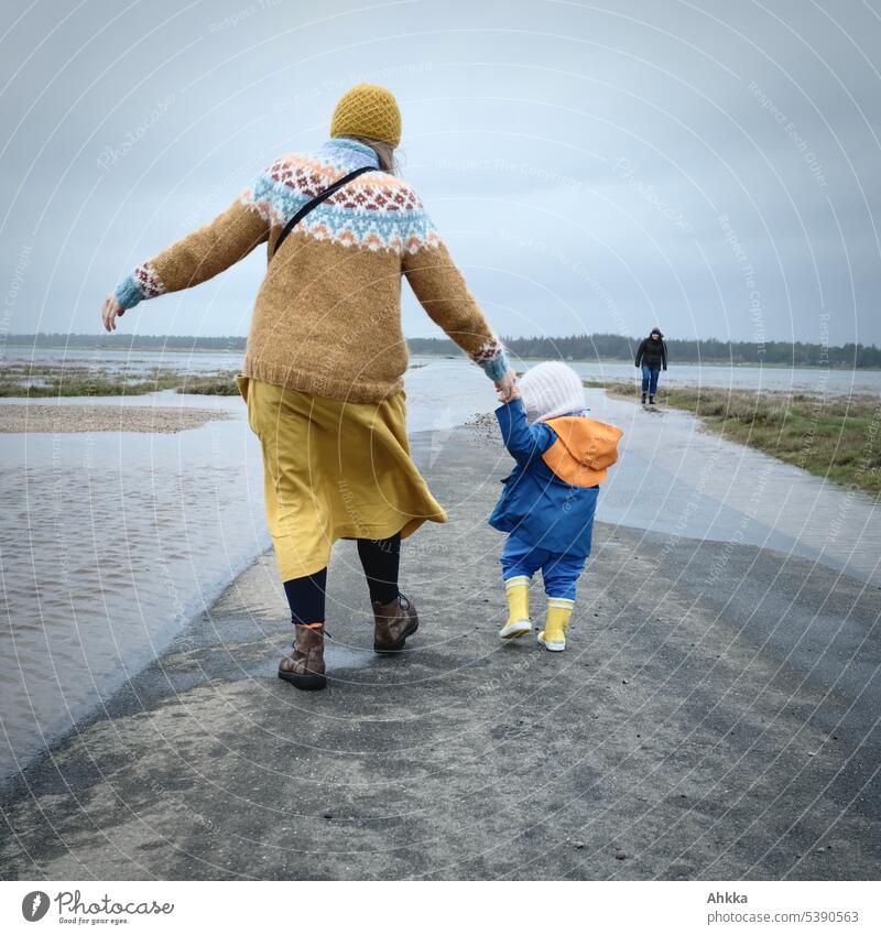 Young woman with small child in yellow and blue on a flooded road on the coast Toddler Gale Street Water flooded street Extreme Walking Flood