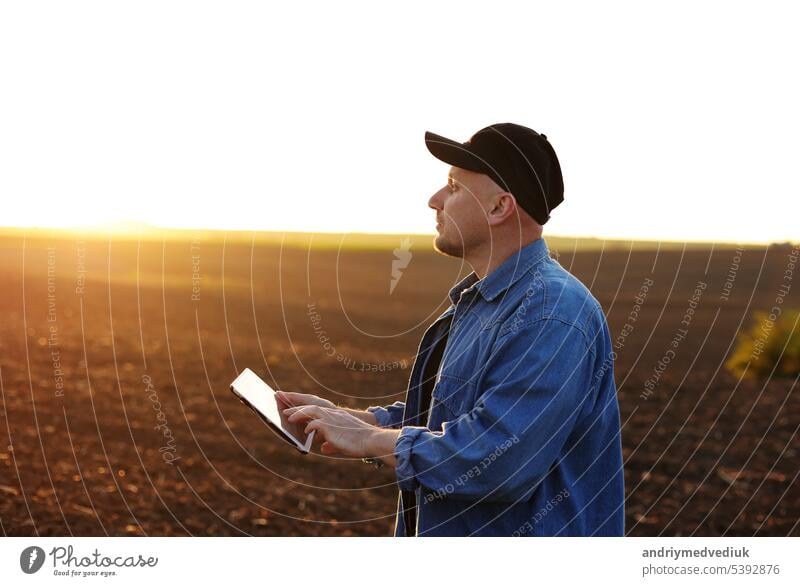 Smart farming technology and agriculture. Farmer uses digital tablet on field with plowed soil at sunset. Checking and control of soil quality, land readiness for sowing crops and planting vegetables