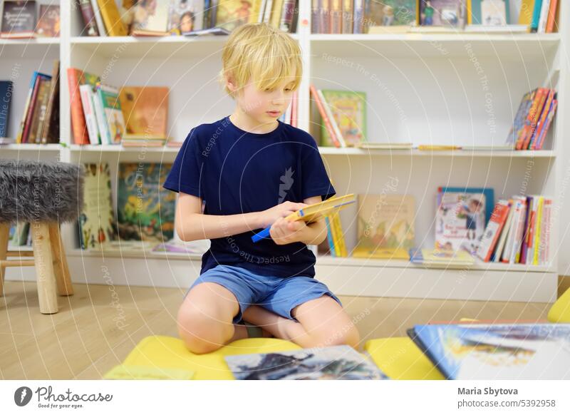 A preteen boy leafing through a book while sitting at the bookshelves in a school library or bookstore. Smart kid reading adventure book child skills lesson