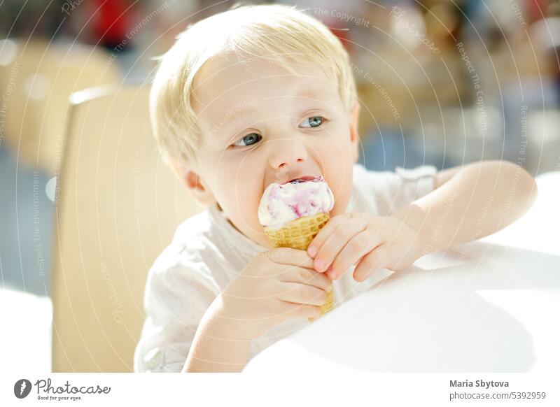 Cute little boy eating ice cream in a waffle cone. Child is tasting gelato in Italian cafe. Unhealthy street fast food. ice-cream child icecream italian