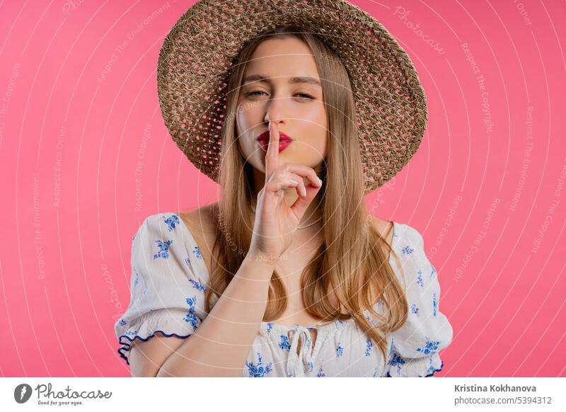 Smiling woman with finger on lips - shhh, secret, silence,pink studio background asking biting charming closeup concept conspiracy contemplation cute decision