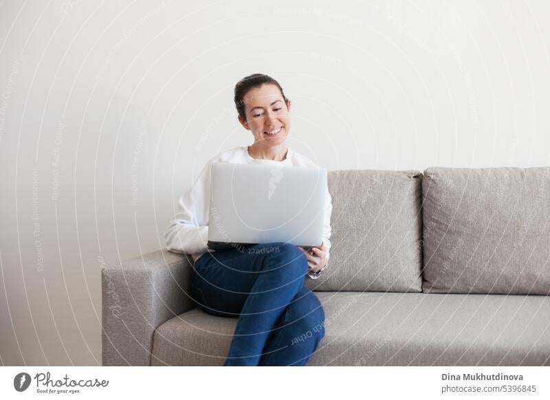 Young woman working on laptop. Millennial girl working remote job from home, sitting on the cozy sofa, smiling. background beautiful business casual caucasian