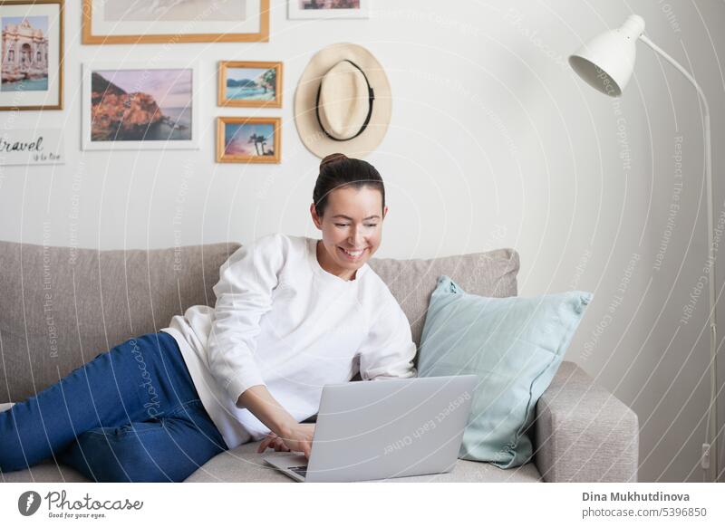 Young woman working on laptop. Millennial girl working remote job from home, sitting on the comfortable sofa, smiling. background pretty Business Easygoing
