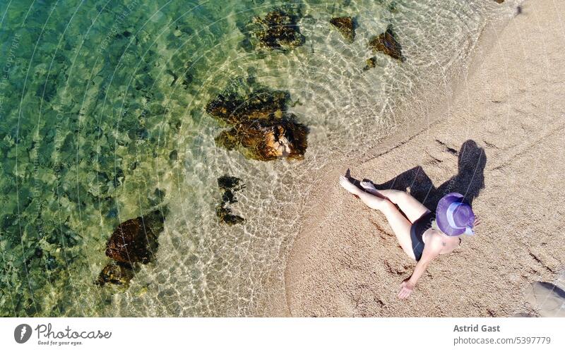 Woman in swimsuit and straw hat sits in the sand by the sea Aerial photograph drone photo Senior citizen vacation Ocean Italy Beach Sandy beach Water stones