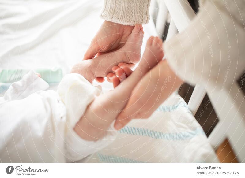 A new mother gently holds her newborn baby's tiny feet in the crib at home hands holding legs premature view diaper subjective little feet little fingers