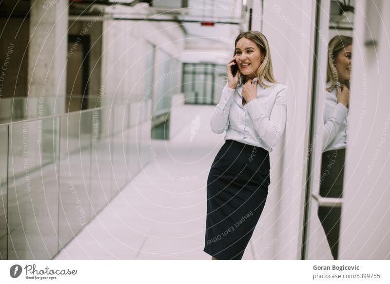 Young business woman using mobile phone in the office hallway caucasian professional businesswoman female people person confident talking cellphone