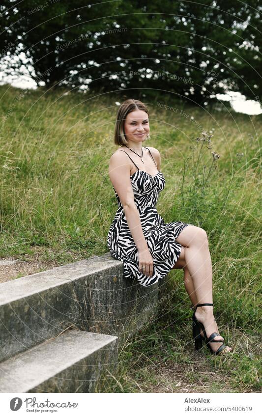 Full body portrait of young woman with makeup on, sitting on concrete rung in black and white striped summer dress and smiling Woman Young woman Face of a woman