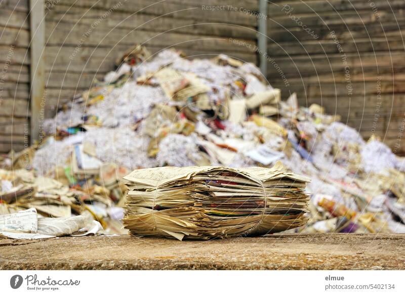 a bundle of newspapers lies in front of a mountain of loose waste paper in a wooden crate / recycling Waste paper Recycling Paper newsprint old newspapers Stack