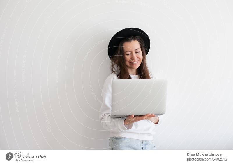 Young millennial woman wearing black hat using laptop, working online, white background. Copy space left and right. beautiful business call caucasian cheerful