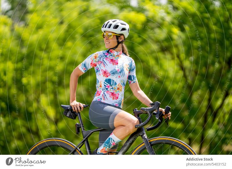 Sportswoman on bicycle against blurred park sportswoman cyclist hardhat sunglasses sportswear fit admire summer female bicyclist athlete racer safety helmet