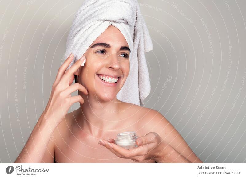 Happy woman with towel wrapped head applying cosmetic mask and cream on face skin care procedure cosmetology routine moisture treat young female rejuvenate