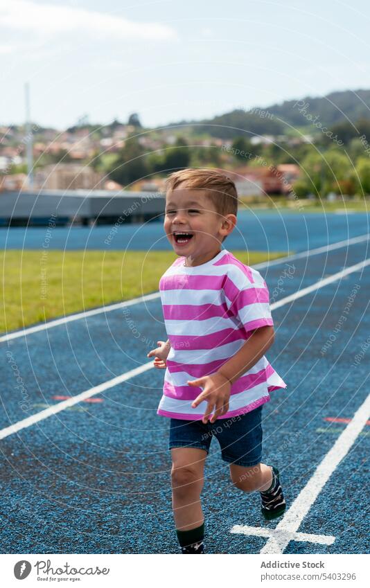 Happy boy running on racetrack in daytime smile happy cheerful laugh child activity sports ground fun energy adorable playful childhood kid joy having fun glad