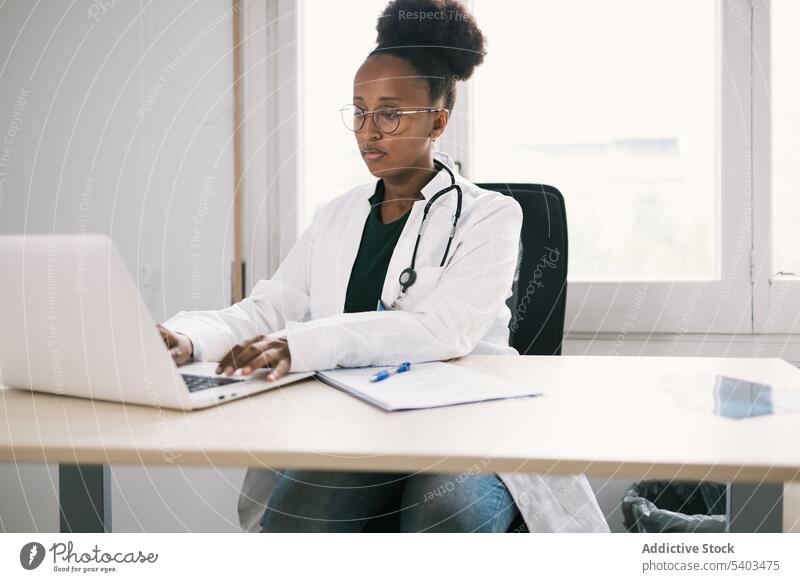 African American physician working on laptop woman doctor practitioner health care table typing medicine using female window uniform lady afro career consultant