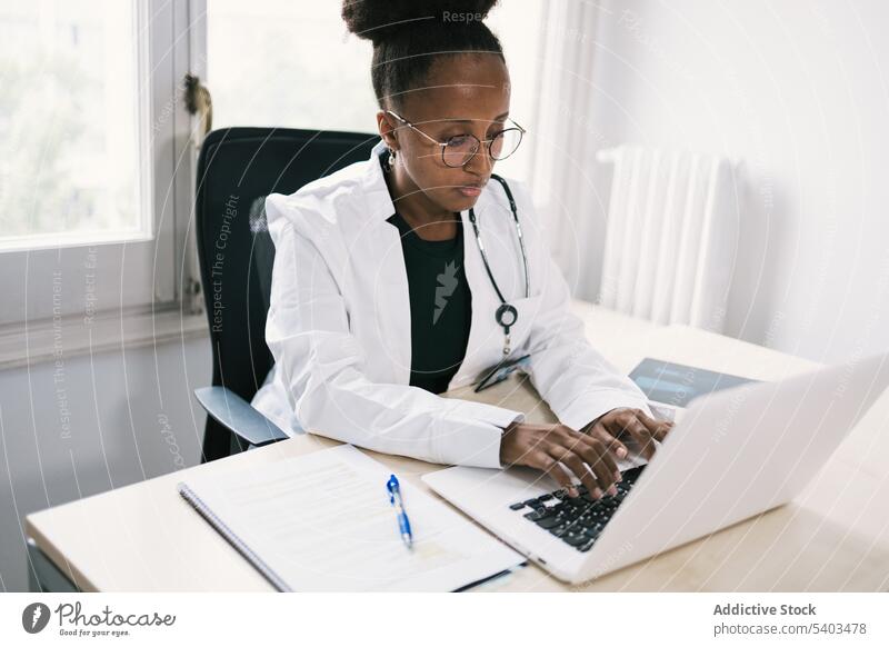 African American physician working on laptop woman doctor practitioner health care table typing medicine using female window uniform lady afro career consultant