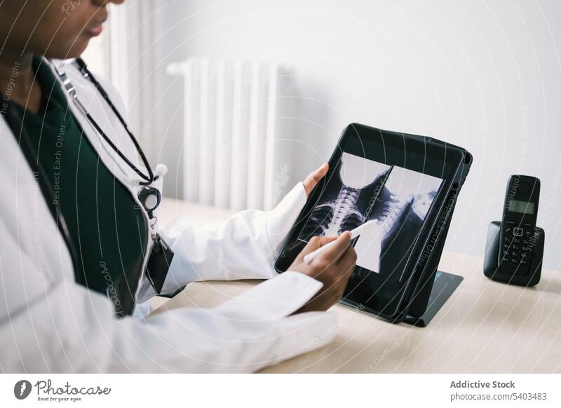 Crop black doctor sitting at table and checking x ray on tablet woman uniform stethoscope specialist professional room female ethnic african american gadget