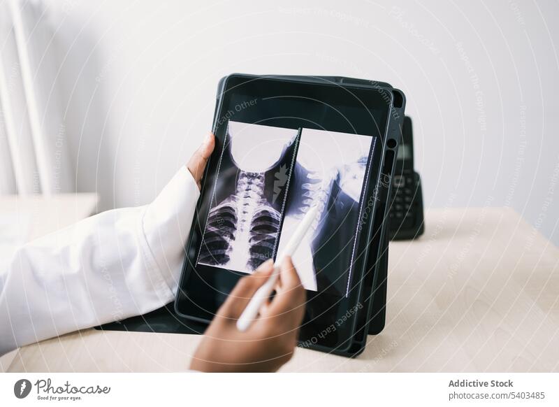 Crop black doctor sitting at table and checking x ray on tablet woman uniform specialist professional room female ethnic african american gadget device clinic
