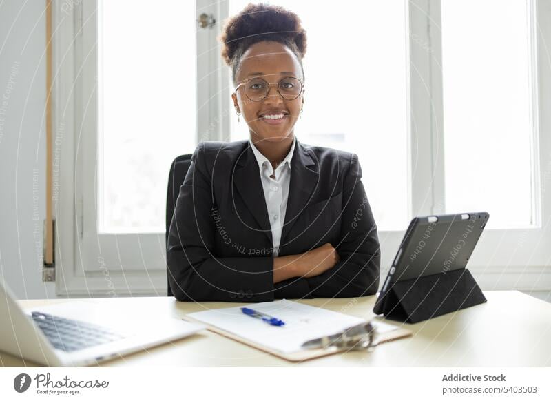 Happy black businesswoman sitting at table and looking at camera entrepreneur smile professional hands crossed positive glad pleasant workplace office young
