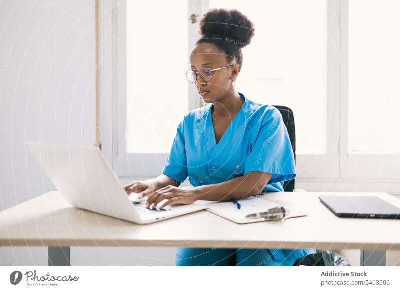 Black woman doctor sitting and working on laptop concentrate online focus uniform professional workplace young female ethnic african american black tablet