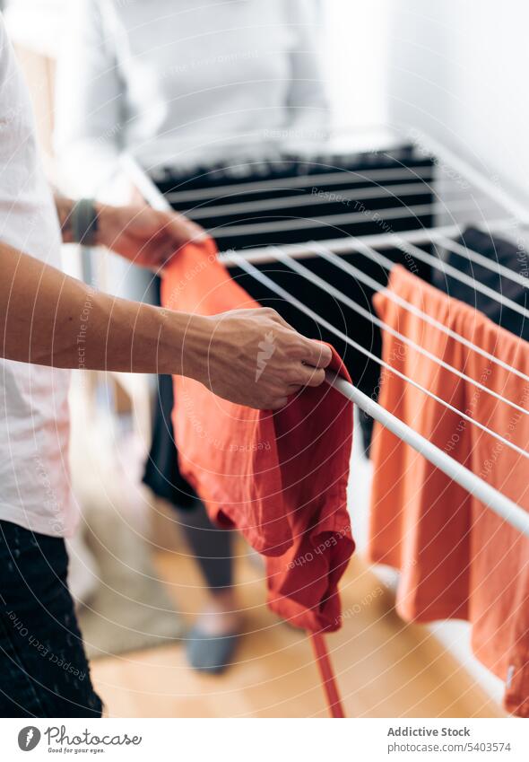 Crop man in casual clothes hanging clean clothes near crop woman in room at home adult clear clothing domestic life dry drying fold garment grip homework