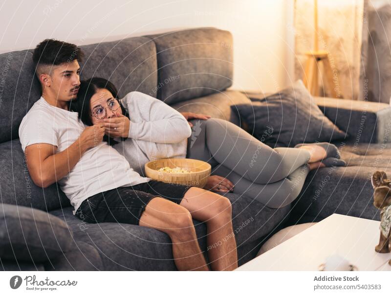 Couple at home watching scary movie with popcorn apartment caucasian comfortable couple date daytime eating film flat girl guy house indoor inside lady