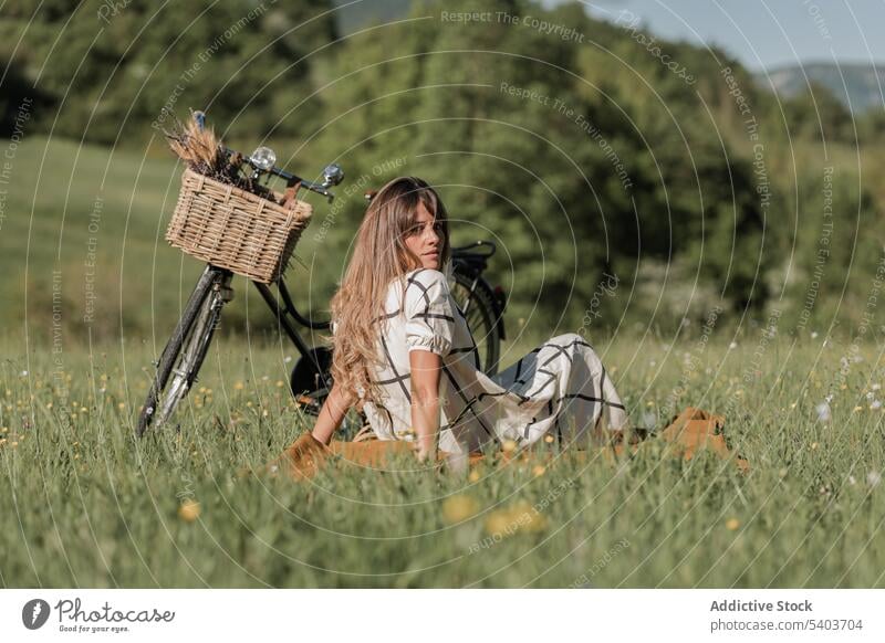 Serious young woman with bicycle on grassy field rest countryside weekend nature relax enjoy sit female peaceful casual carefree recreation blanket lifestyle
