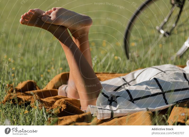 Crop woman lying on grass relax summer field tourist vacation rest barefoot holiday female young blanket bike bicycle nature recreation chill calm harmony enjoy