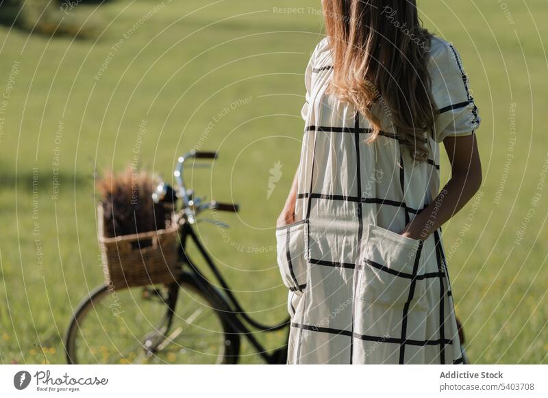Faceless woman with bicycle on grassy field flower basket nature dress long hair peaceful young summer countryside female floral lifestyle idyllic lady green