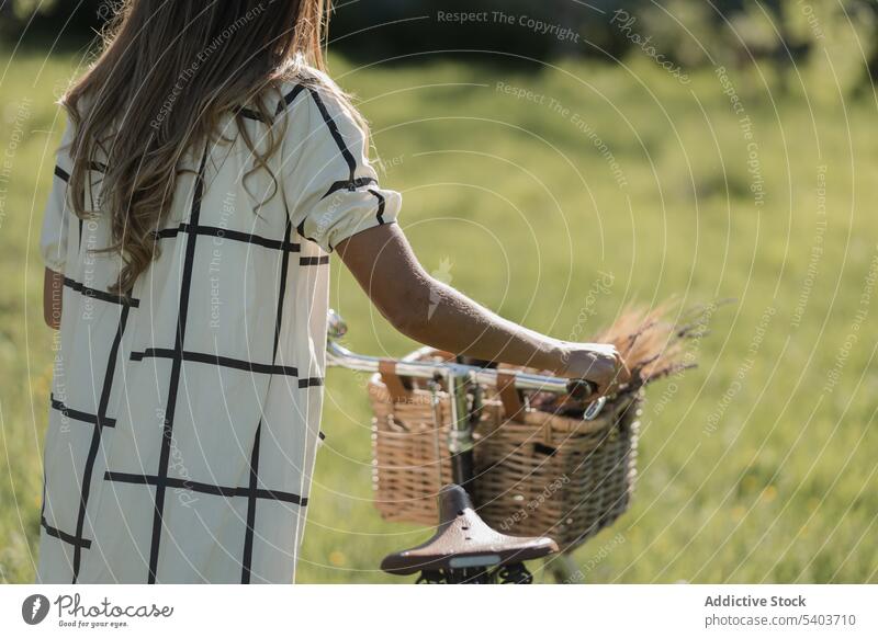 Anonymous young woman with bicycle in countryside field nature casual activity lifestyle grass walk female fresh rural summertime carefree active cyclist