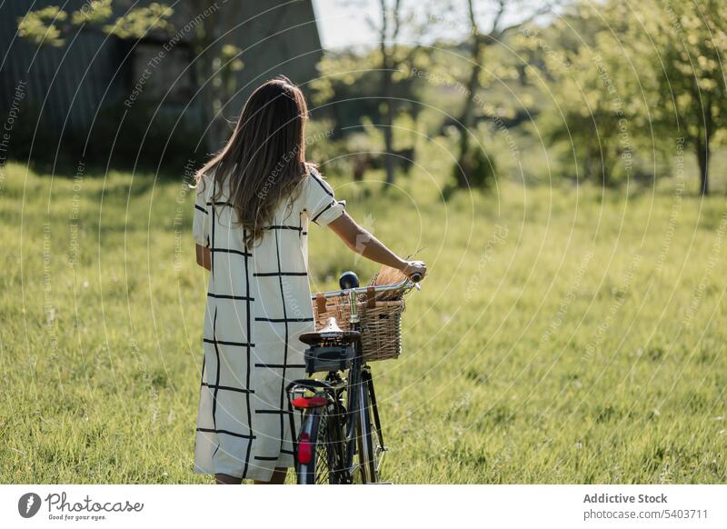 Anonymous young woman with bicycle in countryside field nature casual activity lifestyle grass walk female fresh rural summertime carefree active cyclist