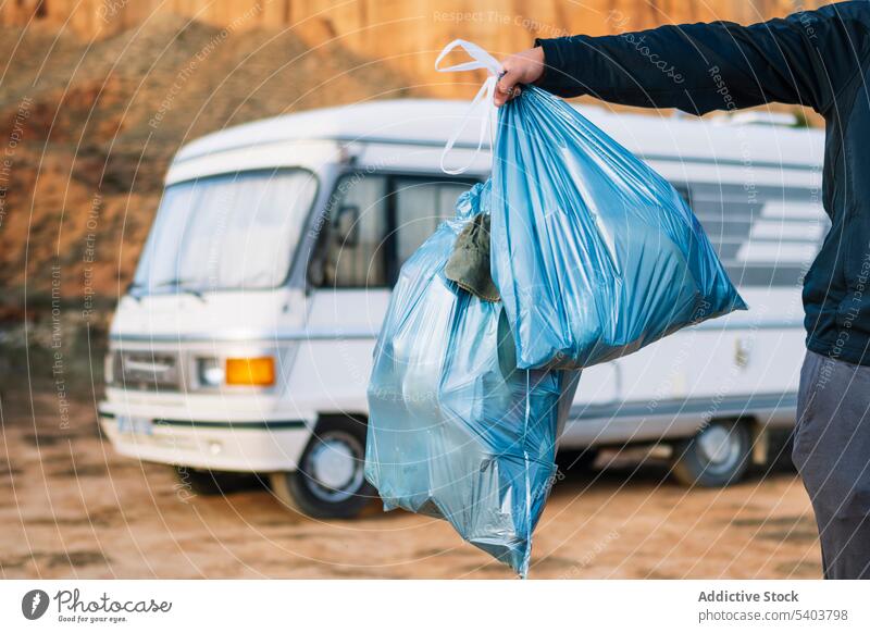 Crop traveler with plastic trash bag by camper van person nature waste hill vehicle sunlight collect rubbish care vacation camping trip rojo teruel stand sand