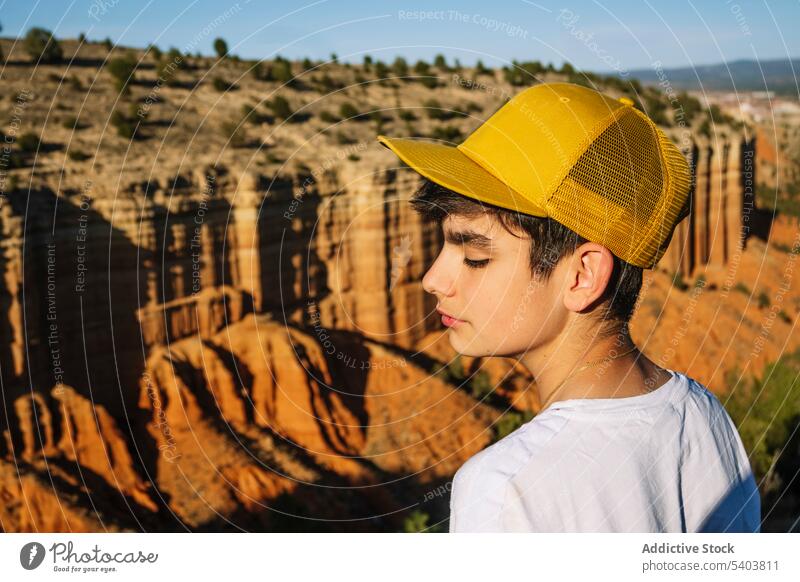 Pensive boy in cap standing above canyon mountains nature landscape thoughtful tourist trip eyes closed rock calm rojo teruel pensive observe cloth male casual