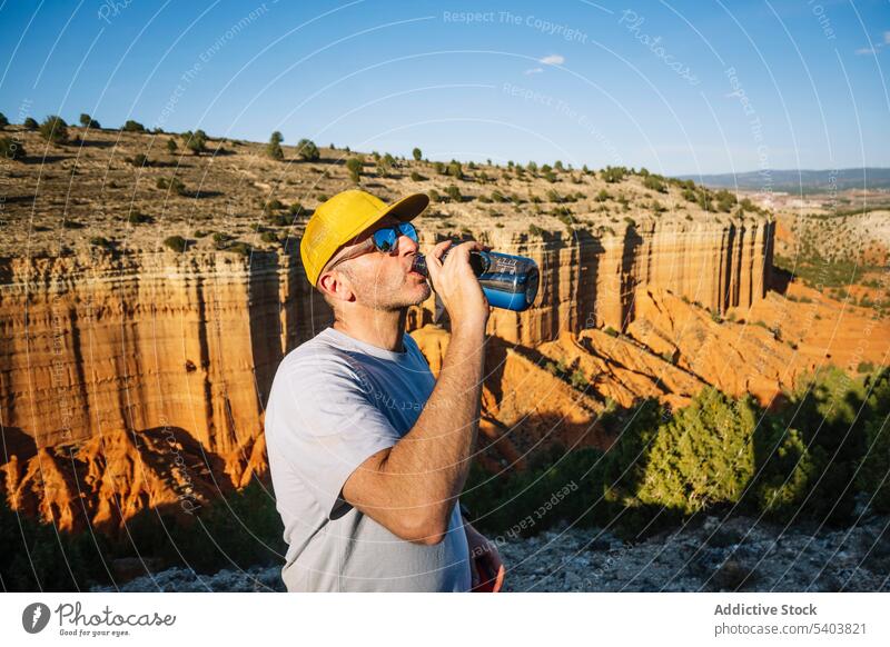 Man drinking water from bottle while standing by cliff man canyon tourist mountain refreshment rojo teruel spain adventure cap male summer sunglasses travel