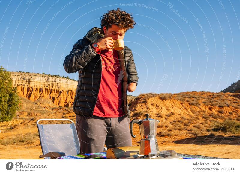 Man with amputated arm drinking hot beverage in campsite man coffee nature travel tourist vacation tourism amputee hot drink morning traveler freedom