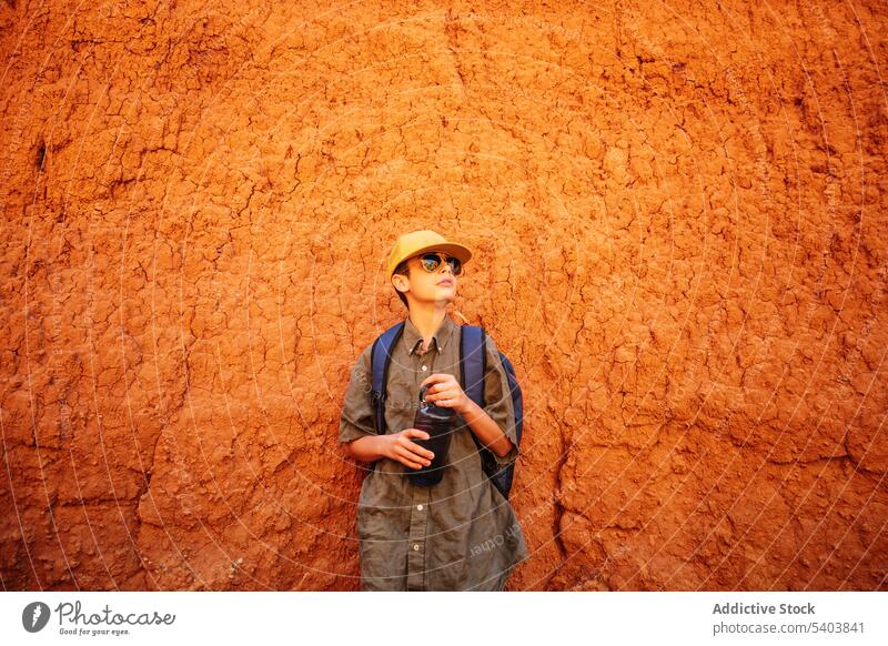 Stylish teenage boy in sunglasses and water bottle standing by sandstone teenager pensive tourist traveler thoughtful limestone tourism canyon journey vacation