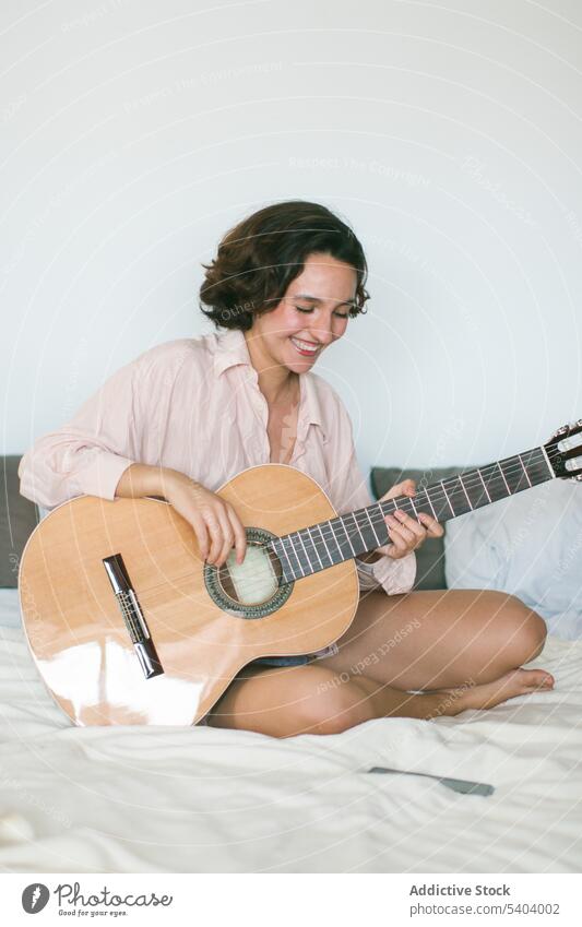 Content young woman with closed eyes playing guitar on bed in bedroom music practice acoustic hobby leisure relax home female instrument guitarist melody
