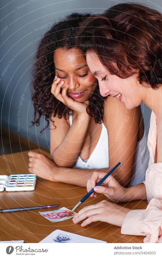 Lesbian couple coloring picture on paper at home lesbian draw together positive happy paintbrush smile women girlfriend table multiethnic multiracial cheerful